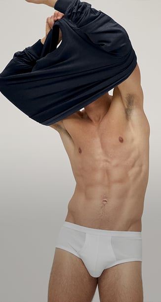 The picture shows a man in white briefs pulling his top over his head.