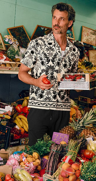 A male model sits on the balcony, coffee in hand, wearing the blue pyjama from the Relax Selected series.