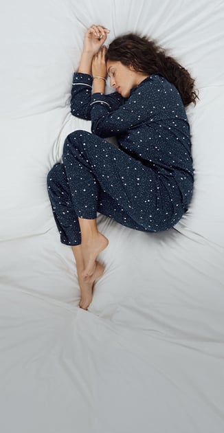 The model is relaxing in bed, wearing pyjamas from the Sweet Dreams series.