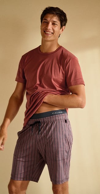 Smiling person in a T-shirt and striped shorts lifting their shirt slightly.