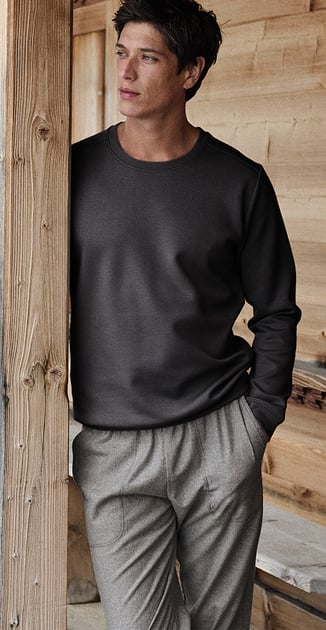 Model trägt ein dunkelgraues Nachtwäsche-Oberteil mit Rundhalsausschnitt und eine graue Loungehose in einer natürlichen Holzumgebung.