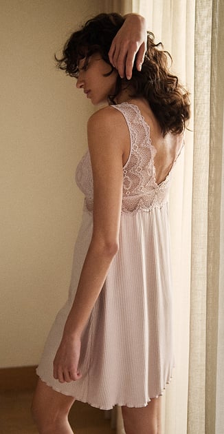 The lady is standing relaxed by the window, wearing a TENCEL™ Modal nightdress from the Feminine Lounge range in rose.