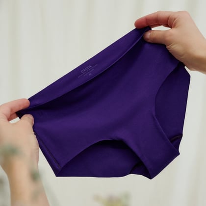 Hände halten eine lila Unterhose aus elastischem Material, Fokus auf der Unterhose.