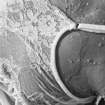Detailaufnahme eines weißen Spitzen-Tops mit transparenter Struktur und Wassertropfen auf der Haut des Models. Bild in schwarz-weiß.