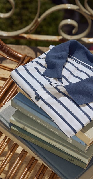 On a stack of books lies the RMX Lounge Journey Polo Shirt in the color Dark Denim.