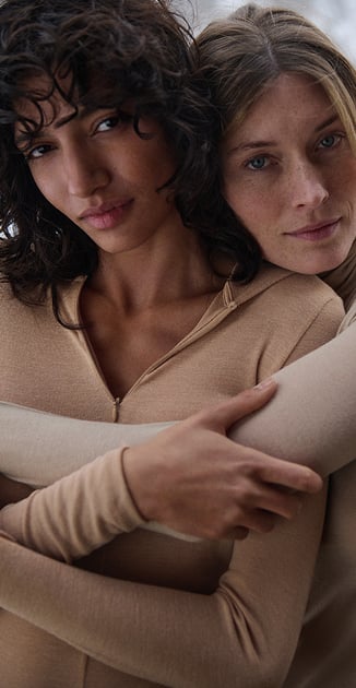Due modelle indossano una maglia a maniche lunghe con cappuccio e una maglia a collo alto in lana e seta della serie True Confidence.