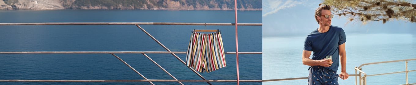The picture shows a Man standing in front of the ocean and wearing a blue summer pyjama.