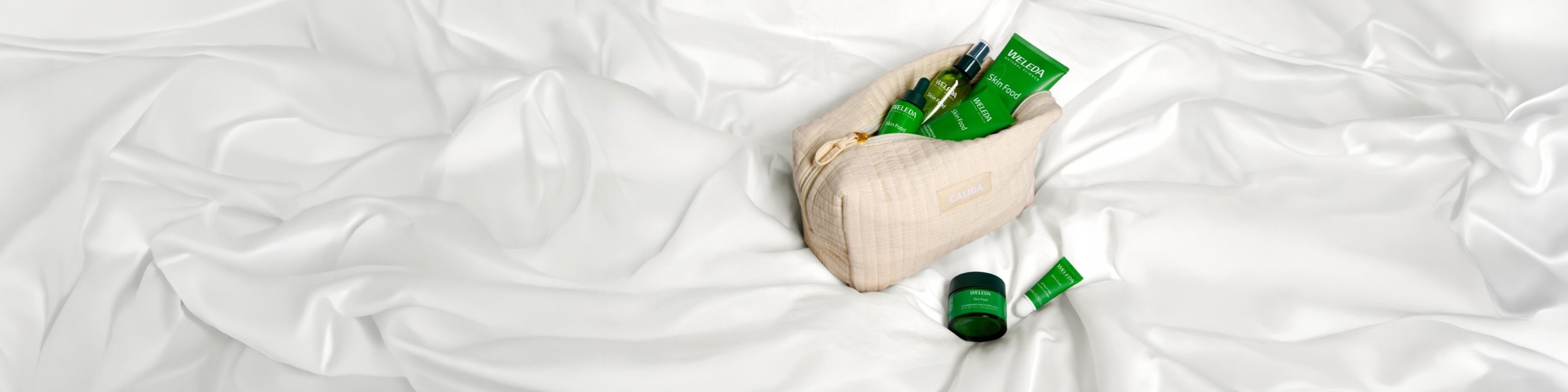 Una trousse su sfondo bianco, piena di prodotti WELEDA.