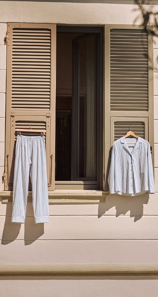 Il pigiama Striped Dreams con bottoni è appeso a una persiana.