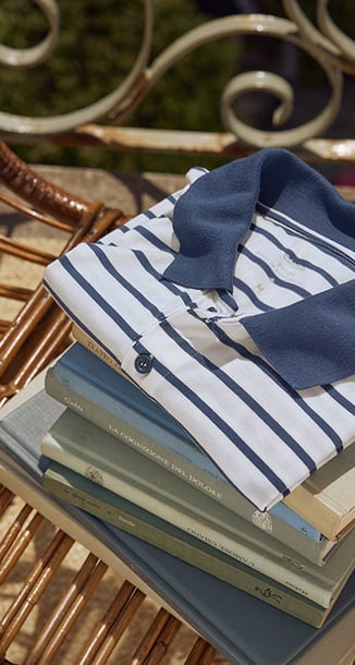 Auf einem Stapel Bücher präsentiert sich das RMX Lounge Journey Polo-Shirt in Dark Denim.