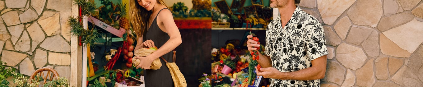 Die Dame und der Herr sind entspannt auf einem Markt, sie trägt den schwarzen Jumpsuit der Serie Favourites Layering und er ein gemustertes Hemd mit passender Bermuda der Serie RMX Lounge Lecce.