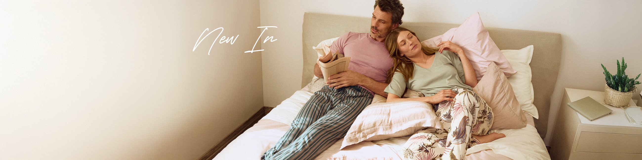 Ein Paar in pastellfarbener Nachtwäsche liegt auf einem Bett und lesen Zeitung