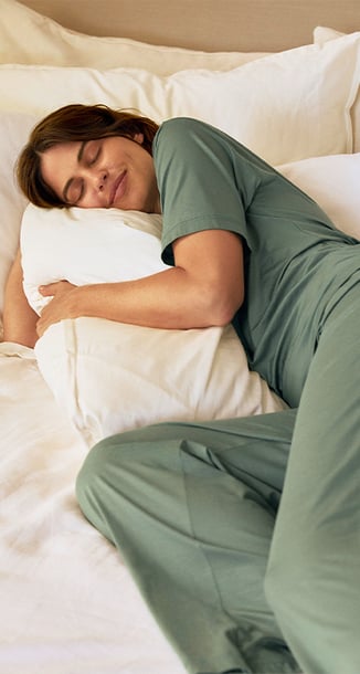Die Dame trägt einen atmungsaktiven Pyjama aus der Serie Deepsleepwear Balancing in der Farbe grün.