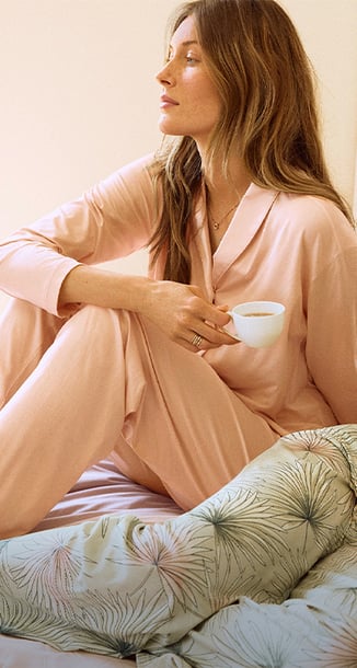 Auf dem Bild sieht man eine sitzende Frau mit einer Espressotasse in der Hand, sie trägt einen Pyjama mit Knöpfen aus der Balancing Dreams Serie von CALIDA.