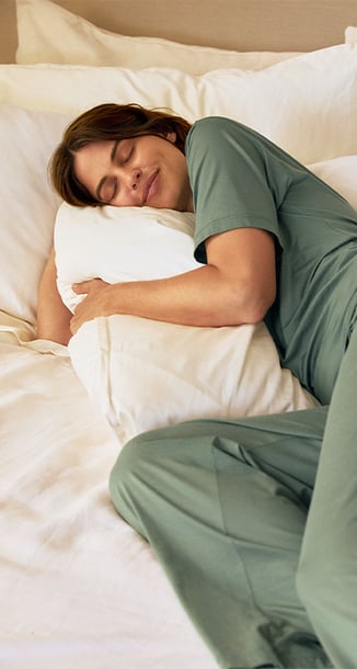 A model lies in bed wearing green pyjamas from the Calida brand.