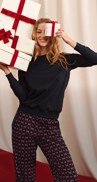 Eine Frau hält viele Geschenke in ihren Händen und trägt einen Pyjama aus der Serie Favourites Holiday.