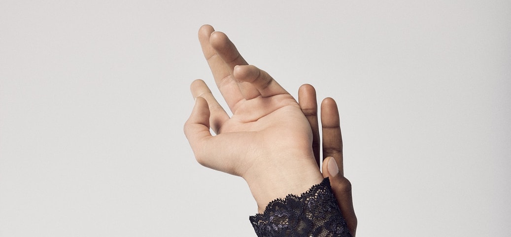 Zwei ineinander verschränkte Hände in eleganten Blusen mit Spitzenärmeln, symbolisch für das Einschlafen oder Taubheitsgefühl der Hände in der Nacht.