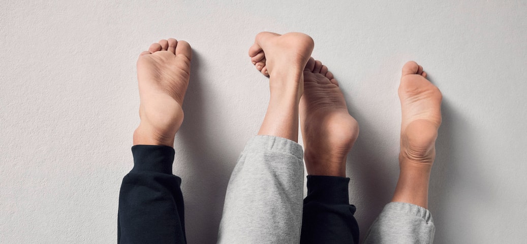Deux paires de pieds nus en pantalon de jogging sont posées côte à côte sur une surface claire.
