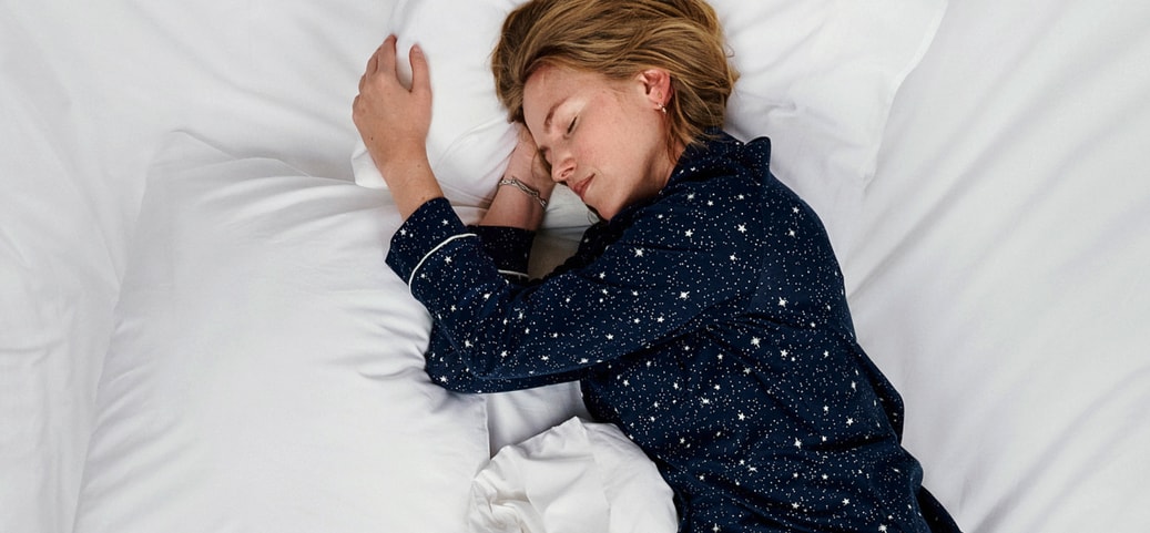 Sleeping person in dark blue star‑patterned sleepwear on a white bed