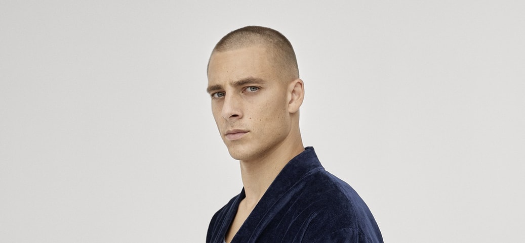 Person wearing a dark blue CALIDA bathrobe from the After Shower collection, standing sideways against a light background.