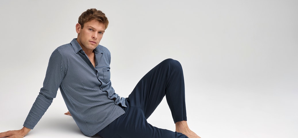 Man in comfortable sleepwear made from breathable fabric sitting relaxed on the floor against a neutral background.