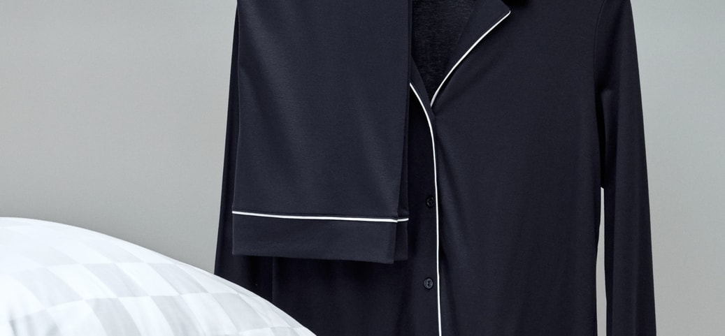 Dark blue CALIDA pyjamas with buttons from the Night Lovers series, neatly displayed on a hanger with pillows