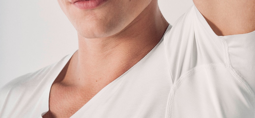 Person wearing a white T‑shirt with one arm raised; symbolic image highlighting the underarm area and the topic of removing deodorant stains