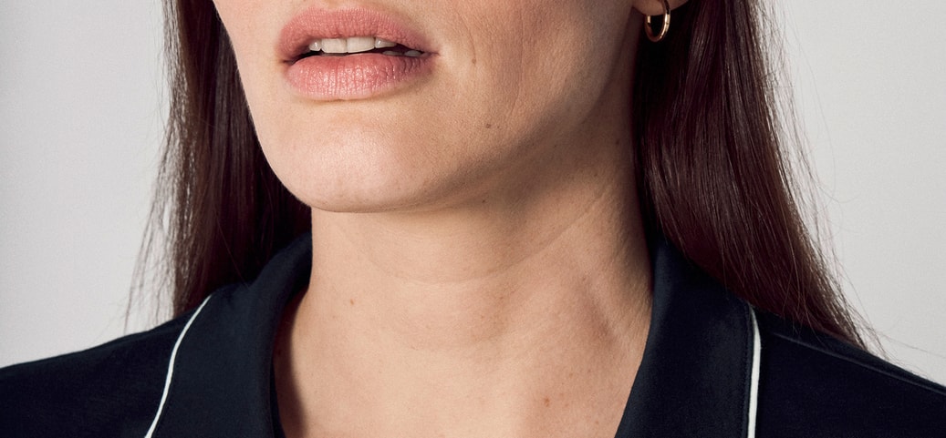 Portrait d'une femme aux yeux fermés et à l'expression neutre, présentant des ridules et des changements cutanés – signes typiques pouvant apparaître pendant la ménopause en raison des fluctuations hormonales.
