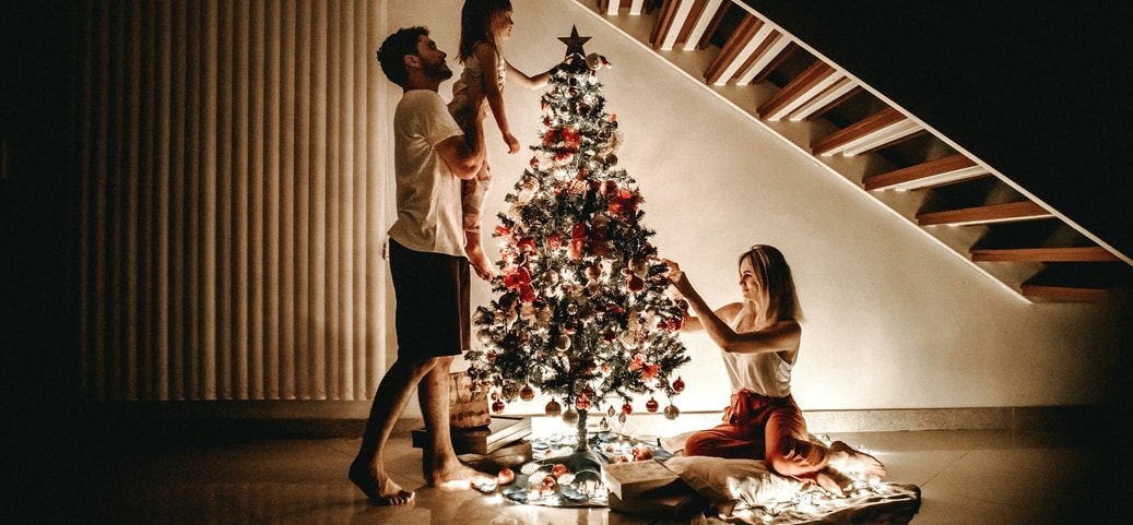 Family decorating a Christmas tree under a staircase – symbol of global Christmas traditions and shared celebration