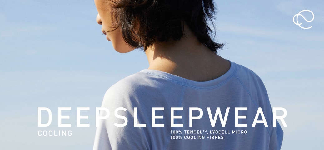 Rear view of a person wearing a light blue DEEPSLEEPWEAR short‑sleeve shirt by the sea, with overlaid text highlighting cooling TENCEL Lyocell sleepwear for menopause.