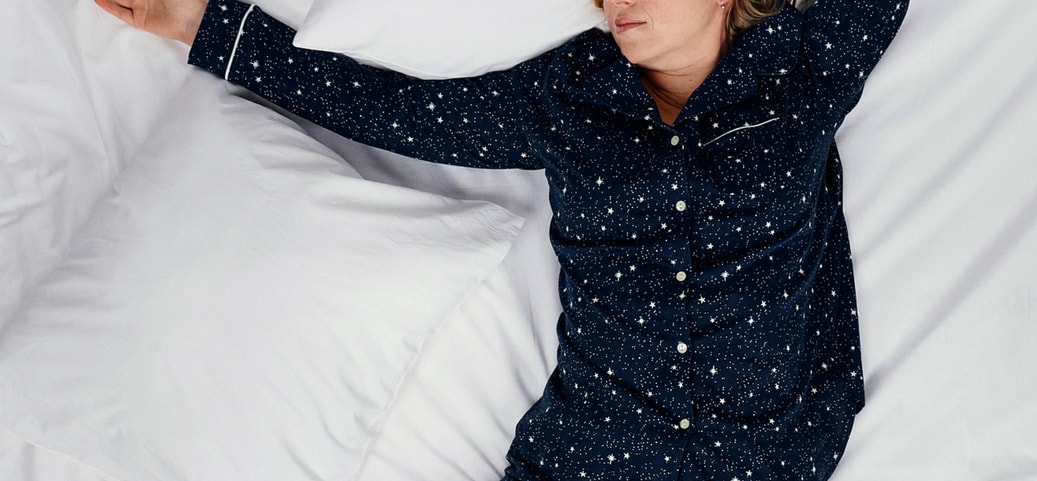 Personne endormie en pyjama bleu foncé à motifs d'étoiles sur un lit blanc ; image symbolique pour le sujet de sensation de froid et de sueur en même temps pendant la nuit