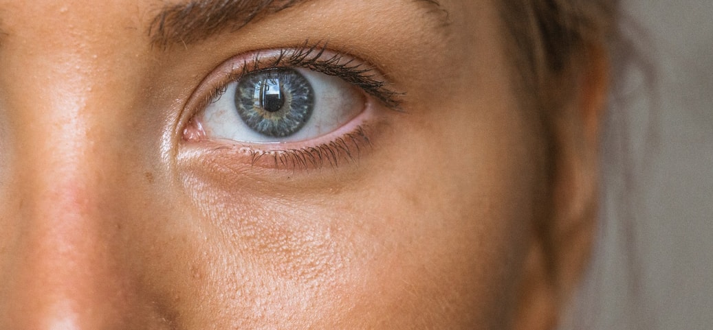 Close‑up of a woman’s eye with a blue‑grey iris; fine skin details visible, the woman is wearing contact lenses