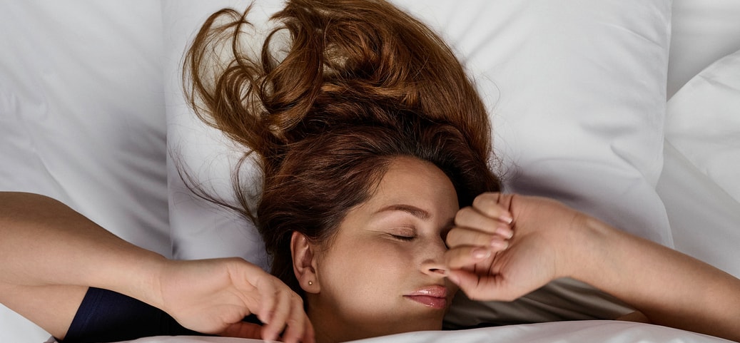 Person liegt unter weisser Bettdecke auf weissem Kissen und schläft entspannt; ruhige Schlafszene als Kontext für Magnesium vor dem Schlaf