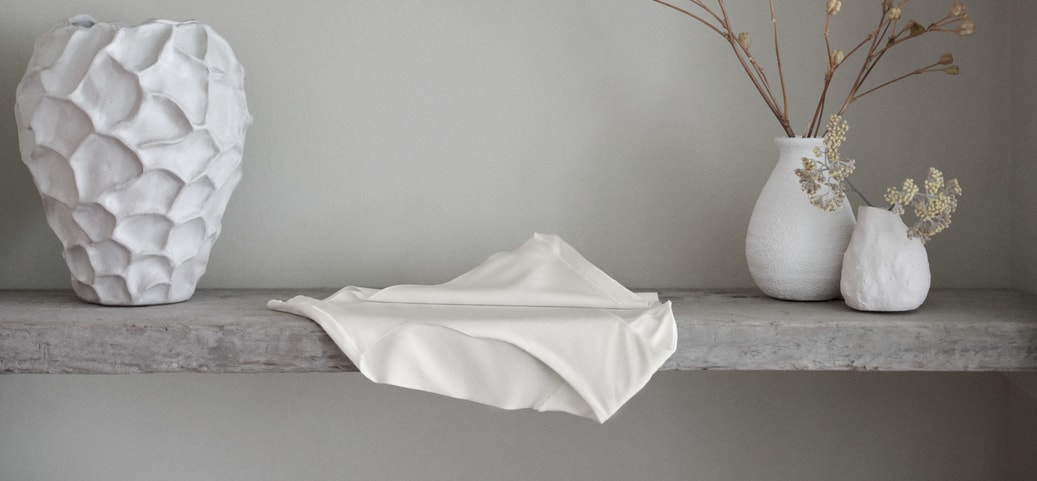 Minimalist decor scene with white vases and fabric on a grey shelf; a CALIDA Seamless Midi Slip from the Natural Skin series placed in the foreground
