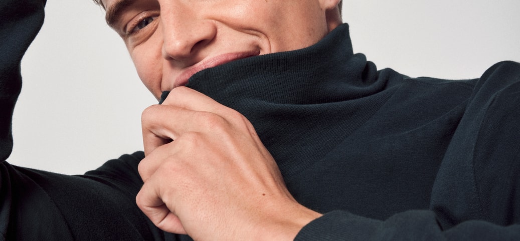 Mann in Basic Loungewear von CALIDA, lächelt entspannt in die Kamera, zieht den Rollkragen seines Oberteils leicht über das Kinn.