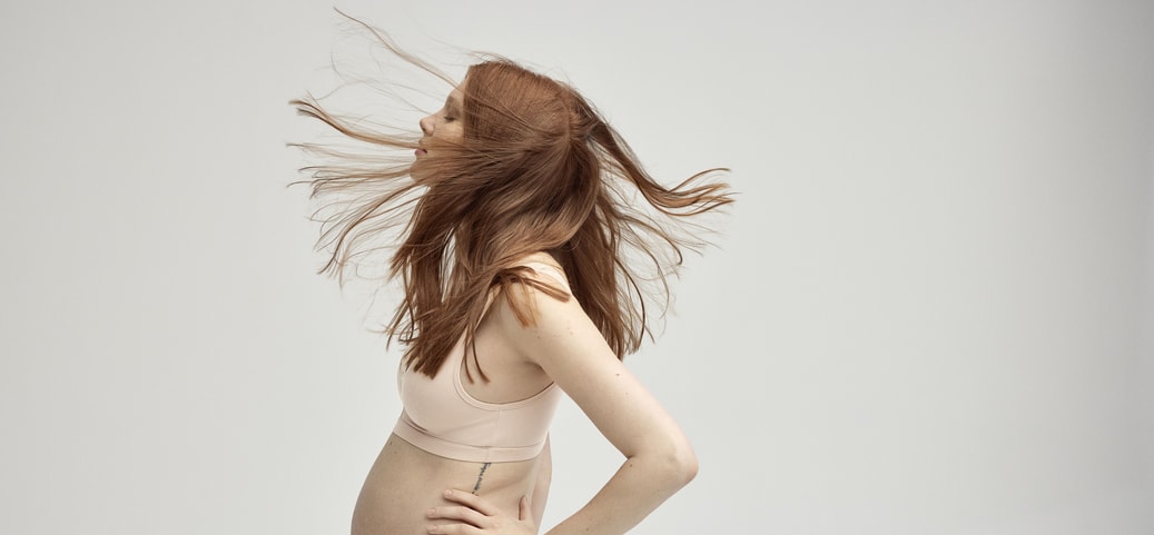 A pregnant woman stands sideways to the camera. Her eyes are closed. She is wearing underwear from CALIDA.
