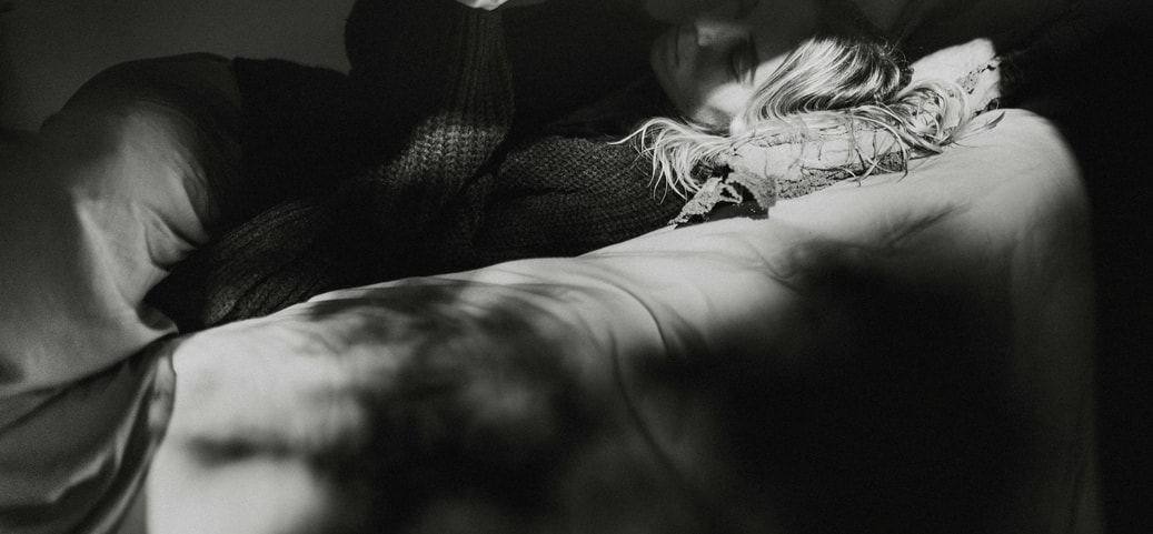 Person lies relaxed in a bed and reads a book in the dim light to calm down and fall asleep better.