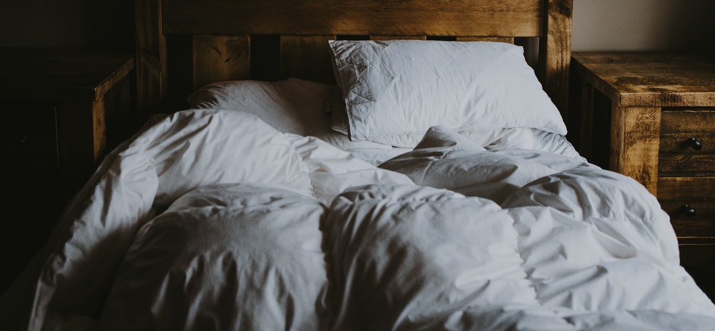 A bed with a white pillow and a white blanket on it.