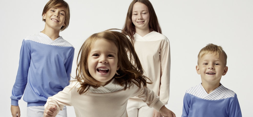 Four children in age-appropriate pyjamas looking happily into the camera symbolise children's need for sleep and the importance of comfortable nightwear for restful sleep