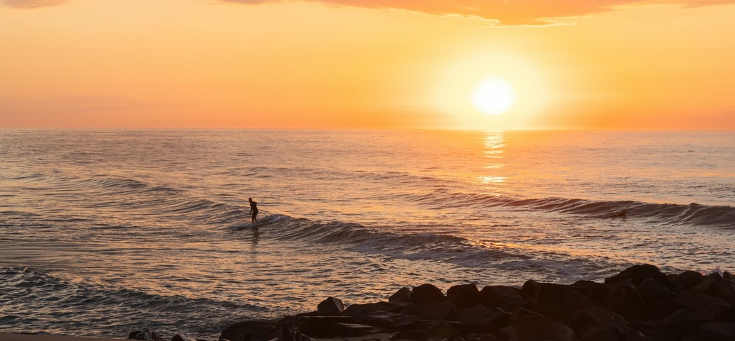 Early morning on the beach, a person stands in the sea as the sun is rising.