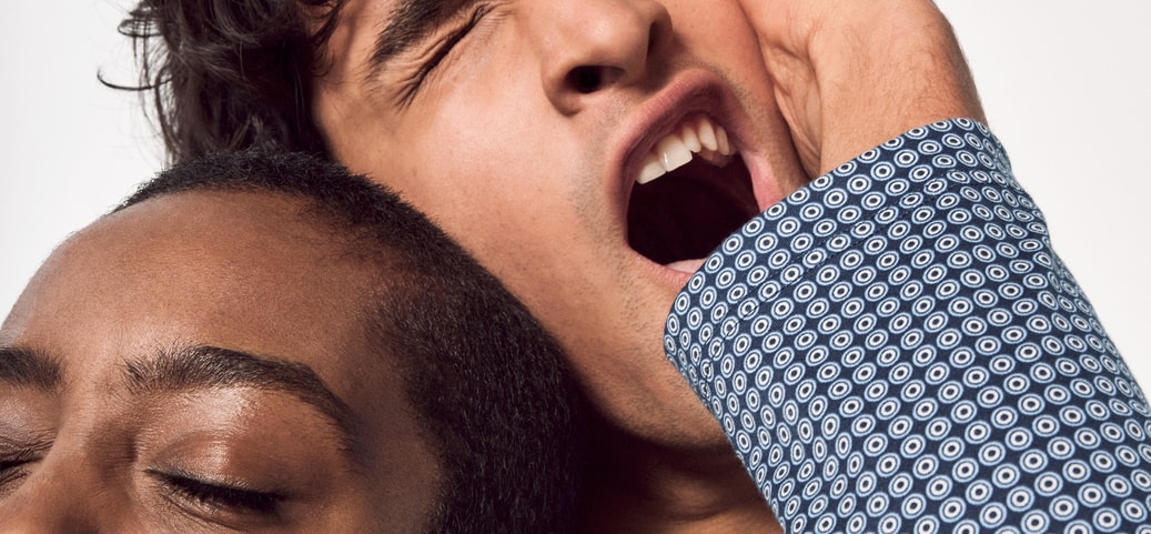 The picture shows a man and a woman in close proximity to each other, both yawning tiredly. The man is leaning his head on the woman's while they are wearing CALIDA pyjamas. The scene conveys a familiar and cosy atmosphere of domestic togetherness.