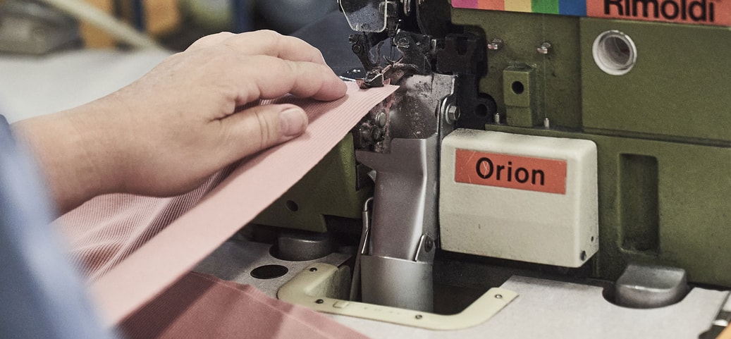 Eine Person repariert kleine Löcher in Kleidung mit einer professionellen Nähmaschine in einer Werkstatt.