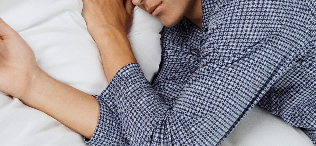 A man lies awake in bed with his eyes closed, answering the question: Why can't I sleep even though I'm tired?