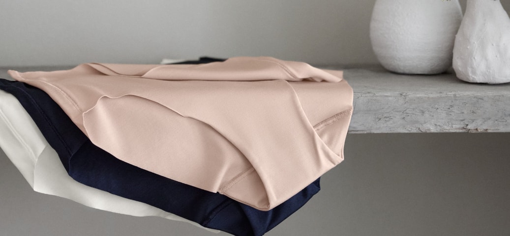 Zu sehen sind drei Pantys von CALIDA aus der Serie Natural Skin in verschiedenen Farben, ordentlich auf einem Regal abgelegt.