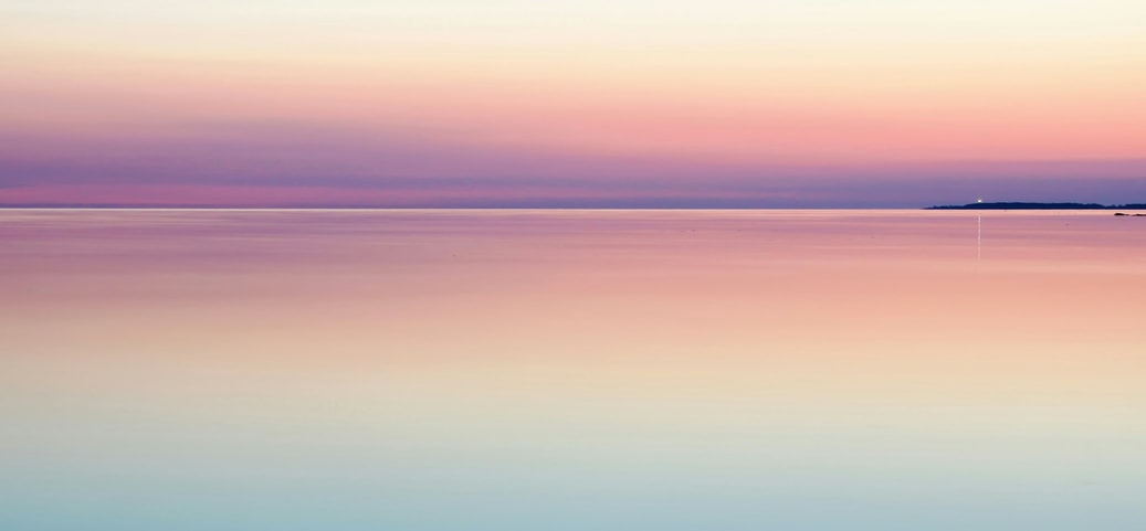 Ein beruhigender Sonnenaufgang über einem stillen Ozean, mit sanften Farbübergängen von Blau über Rosa zu hellem Gelb, die den Himmel und das Wasser harmonisch verschmelzen lassen.