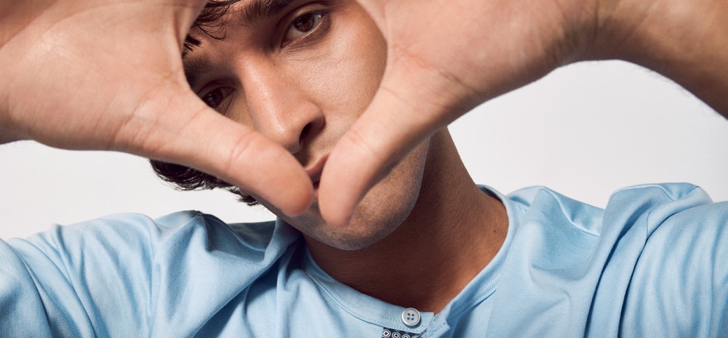 Close-up of a young man in a blue shirt holding his hands in front of his face in the shape of a heart. Symbolises concentration and mindfulness, in keeping with the theme of mindfulness exercises.