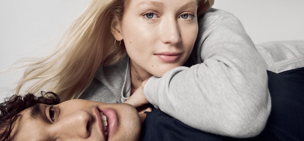 Un couple décontracté en vêtements CALIDA, présentant le Zwiebellook. La femme porte un pull gris, l'homme un haut foncé, tous deux ont l'air sereins et stylés.