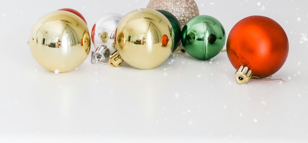 Weihnachtskugeln in verschiedenen Weihnachtsfarben, darunter Gold, Rot, Grün, Silber und Glitzer auf einem weißen Hintergrund, mit einem dezenten Schneeflocken-Effekt.