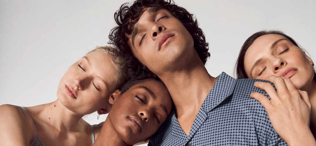 A group of four people with their eyes closed lean against each other as if they were asleep. The scene conveys calm and relaxation. Can you sleep standing up?