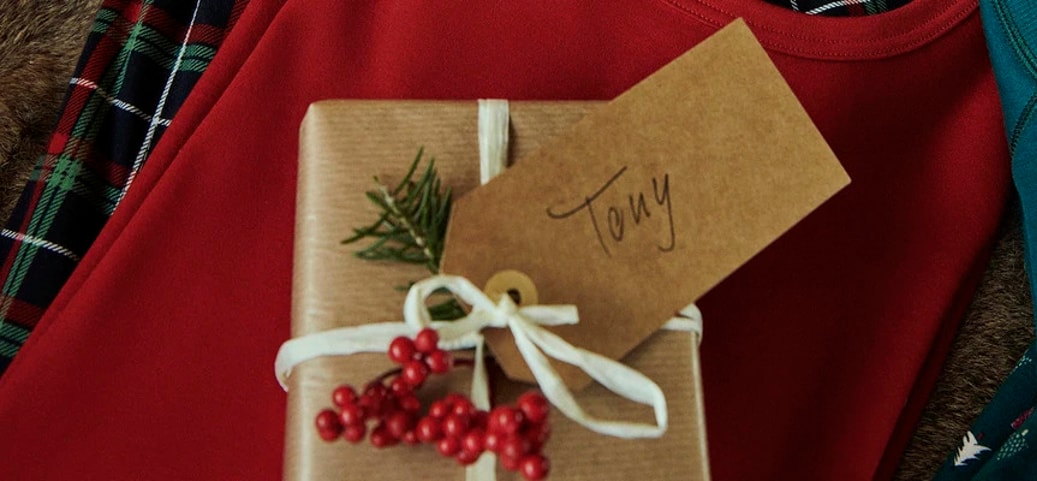 Kleines verpacktes Geschenk mit dem Namensschild 'Tony'. Das Geschenk liegt auf Pyjamas von Calida.